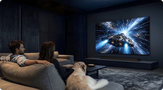 Et par og hunden deres ser på film i et mørkt rom.