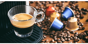 En kop espresso fra en kapselkaffemaskine med kapsler og kaffebønner på disken