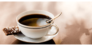 En kopp med svart kaffe och en kaka vid sidan på kaffefatet.