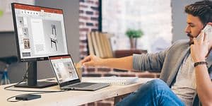 Man sitter och jobbar vid ett skrivbord på en bärbar dator och pratar i telefon samtidigt. 