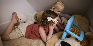 Två barn ligger i myshörna och använder en iPad med Orlando-fodral