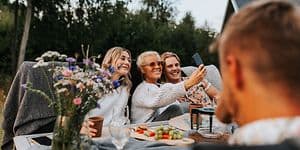 Två tjejer och en pojke tar en selfie i trädgården medan de sitter runt ett bord.