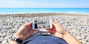 En man som ligger på stranden och tittar på sina övervakningskameror hemma