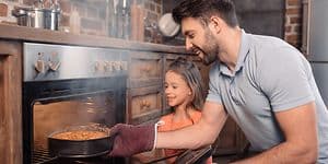 Father and daughter taking cake from oven
