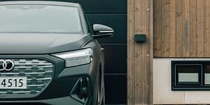 Väggmonterad Amina billaddare bredvid en bil som står parkerad framför ett garage