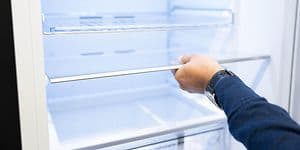 En mands hånd der holder en hylde i et køleskab