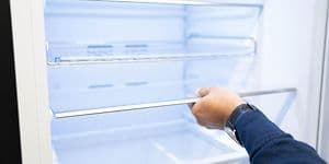 Man's hand holding the shelf of a fridge