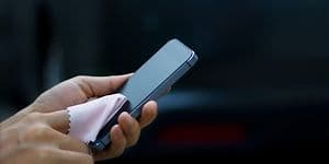 Person holder smarttelefon og rengjør skjermen med en pusseklut