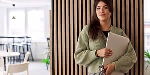 Toimistossa seisova nainen pitelee kannettavaa tietokonetta kädessään