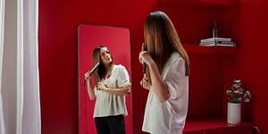 Suoristusrauta - Testivoittaja - Peilin edessä oleva nainen suoristaa hiuksiaan suoristusraudalla