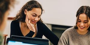 Nuoret naisopiskelijat istuvat opiskelemassa kannettavilla tietokoneillaan