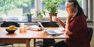 Computing - AI PC - Older woman sitting by kitchen table using her laptop