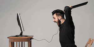 Man med ett tangentbord i högsta hugg, på väg att slå det i datorn som står framför på ett bord. 