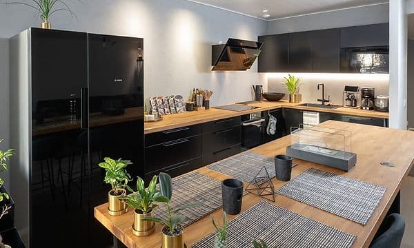 Træbordplade med dækservietter, planter og sortkøkken facade i baggrunden