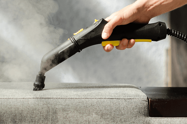 Damprenser med et tekstilmundstykke bliver brugt på en sofa