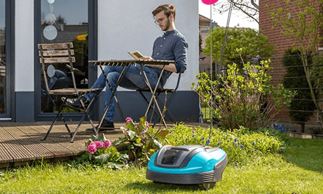mann sitter på stol og leser i hagen med robotgressklipper på gressplen