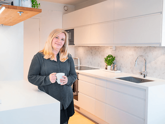 smilende kvinne med kaffekopp står på hvitt kjøkken fra epoq