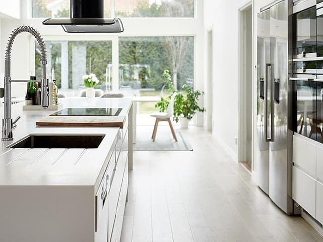 Vitt kök som är stort, öppet och ljust. En köksö med diskho och induktionshäll.