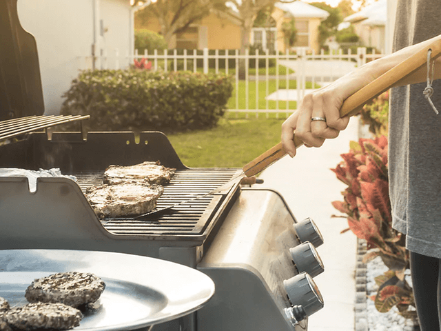 person griller hamburger ute i hagen på gassgrill
