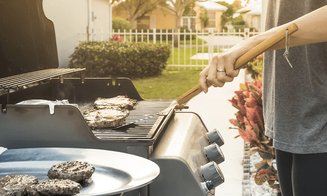 person griller hamburger ute i hagen på gassgrill