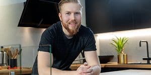 Punahiuksinen mies, taustalla mustat kaapit ja keittiövälineet