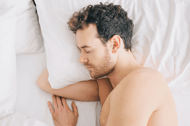 mann sover med arm under pute i en seng