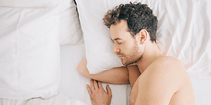 mann sover med arm under pute i en seng