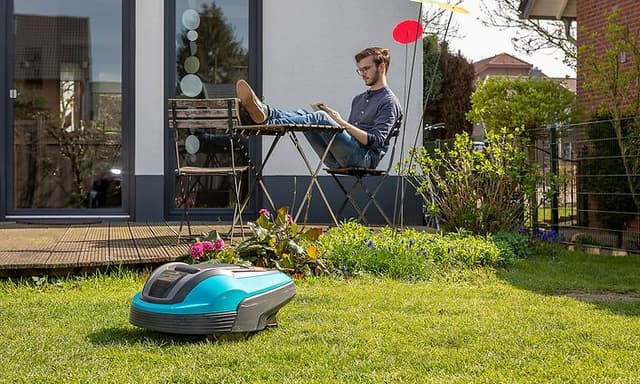 En man sitter och läser i trädgården på altanen medan robotgräsklipparen jobbar med gräsmattan.