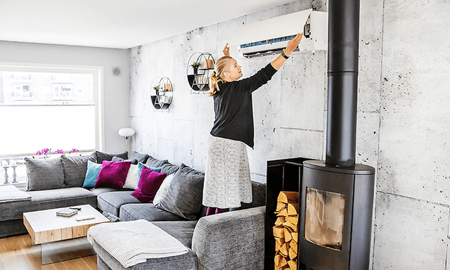 kvinne i stue står i sofa for å undersøke filter på varmepumpe