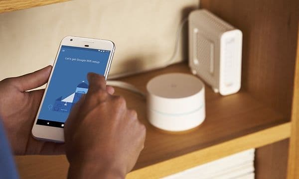 käsittelyssä puhelin, jossa Google WIFI-asetus, taustalla reitittimet
