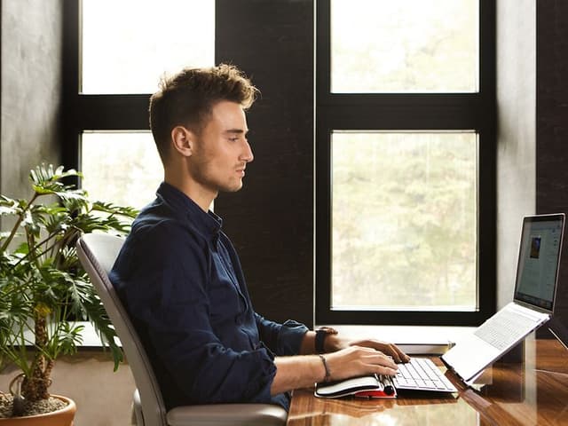 Mies työskentelee kannettavalla tietokoneella. Hänellä on edessään Contour RollerMouse-hiiri ja Balance Keyboard-näppäimistö