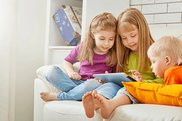 kolme tablettia sohvalla istuvaa lasta käyttämässä tablettia