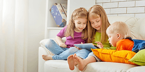 kolme tablettia sohvalla istuvaa lasta käyttämässä tablettia