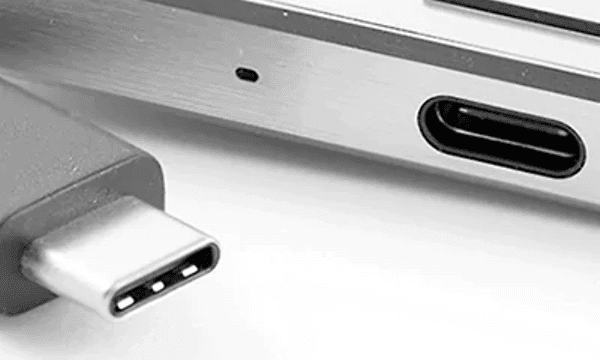Silverfärgad USB-kabel med typ-c anslutning ligger bredvid en laptop med en port som ser ut att passa.