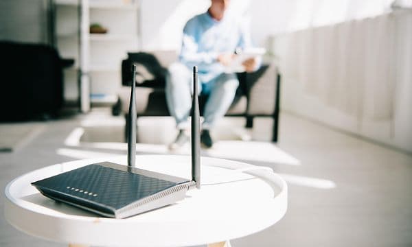 svart trådløs router på bord med mann som sitter i bakgrunnen