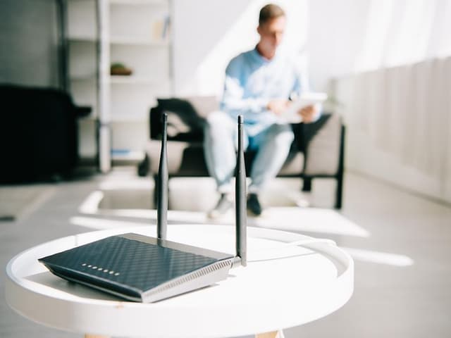 svart trådløs router på bord med mann som sitter i bakgrunnen