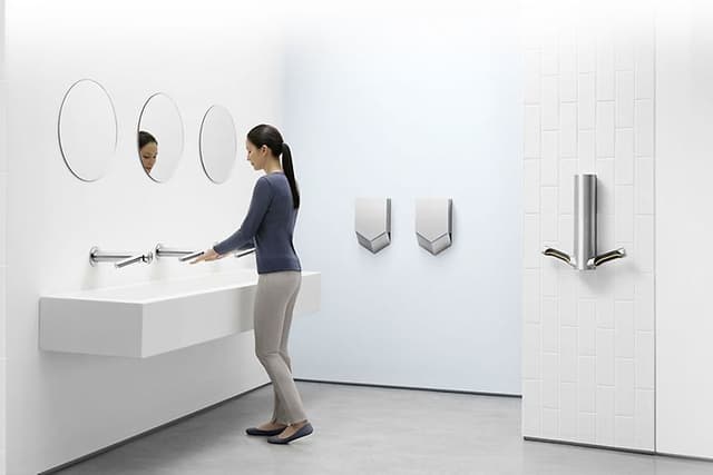 Dyson Airblade -käsikuivaimia wc-tilassa, jossa nainen pesee käsiään
