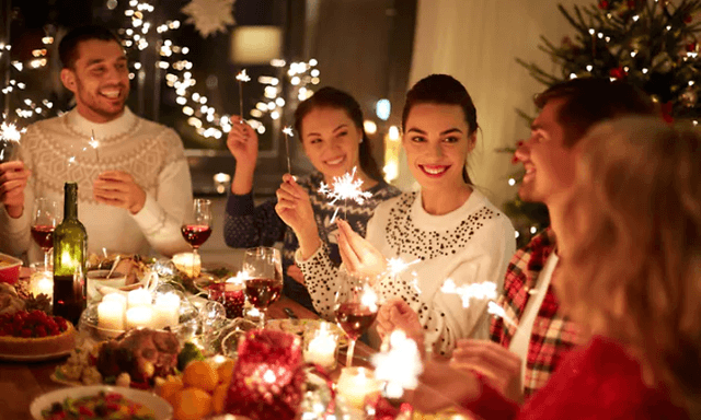 smilende personer rundt et dekket julebord med stjerneskudd i hendene