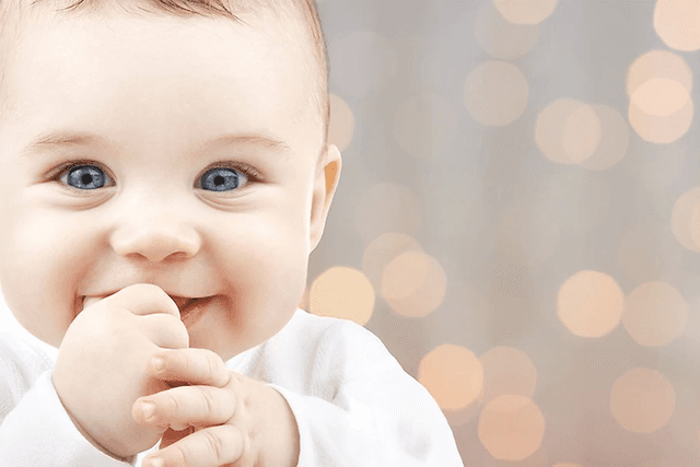 Smilende baby med fingrene i munden