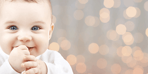 Smilende baby med fingrene i munden