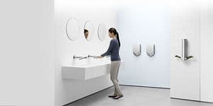 Dyson Airblade håndtørkere montert på vegg på hvitt bad hvor en kvinne vasker hendene