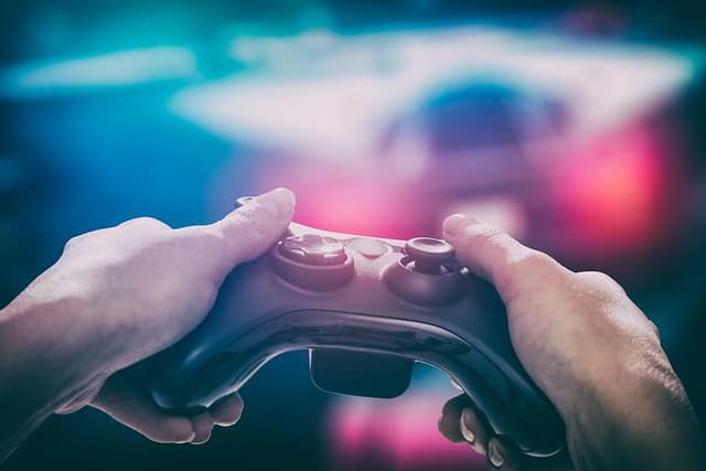 Hænder, der holder controllere, mens personen spiller på en skærm