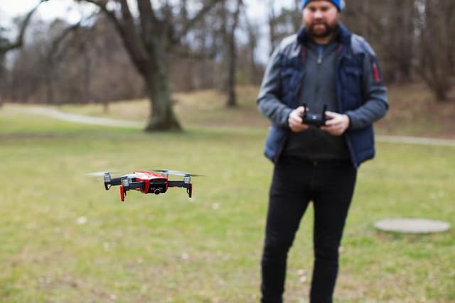 Mand står udenfor, tæt på en skov, og flyver med en drone