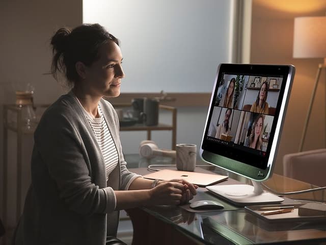 Kvinna sitter vid ett skrivbord och har videomöte med fyra andra personer på en stor skärm. 