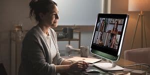 Kvinna sitter vid ett skrivbord och har videomöte med fyra andra personer på en stor skärm. 