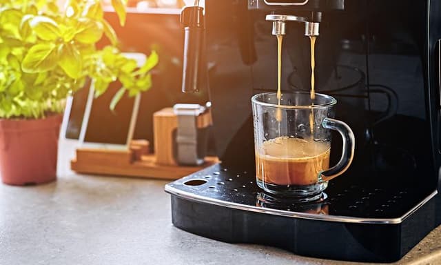 Kaffemaskine der står på et køkkenbord. Kaffemaskinen er igang med at lave en kop kaffe.