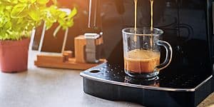 Kaffemaskine der står på et køkkenbord. Kaffemaskinen er igang med at lave en kop kaffe.