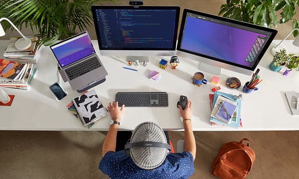 person sitter ved et skrivebord med flere Logitech skjermer og enheter