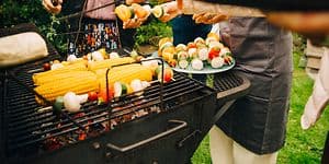 Mennesker som står rundt en kullgrill og lager mat