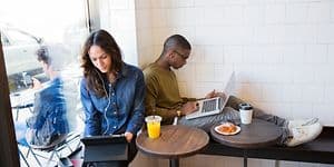 Två personer som sitter på ett kafé med bärbara datorer